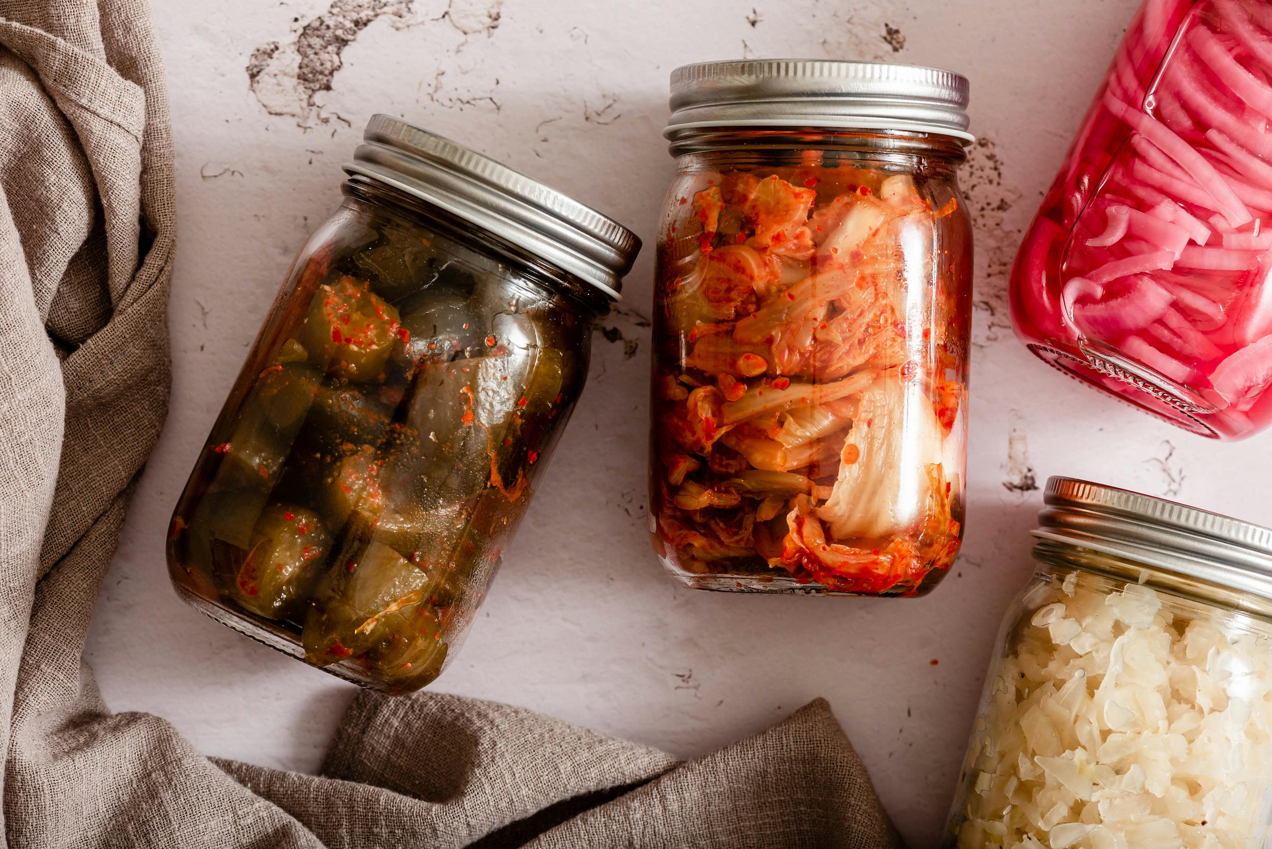 Jars of kimchi, kefir, sauerkraut and kombucha on a kitchen shelf
